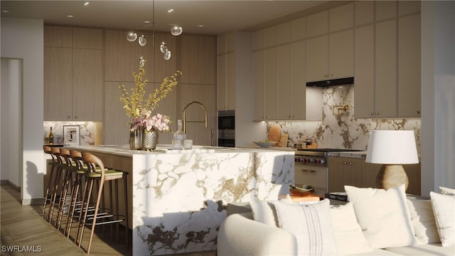 kitchen featuring a sink, stainless steel gas stovetop, decorative backsplash, under cabinet range hood, and a kitchen breakfast bar