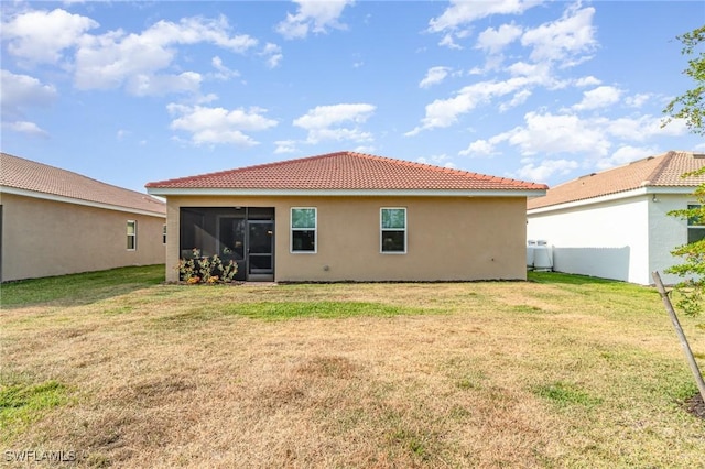 back of house with a lawn, stucco siding, a tiled roof, and a sunroom