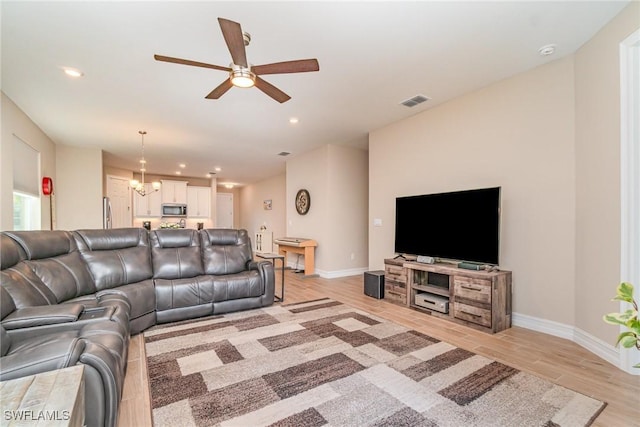 living room featuring light wood-style flooring, visible vents, baseboards, recessed lighting, and ceiling fan with notable chandelier