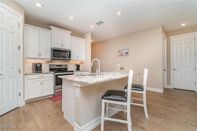 kitchen featuring a sink, appliances with stainless steel finishes, visible vents, light wood finished floors, and an island with sink
