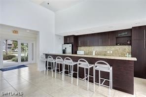 142 Santa Clara Dr Unit 7, Naples, FL 34104 - kitchen with dark brown cabinetry, a breakfast bar, light countertops, freestanding refrigerator, and tasteful backsplash