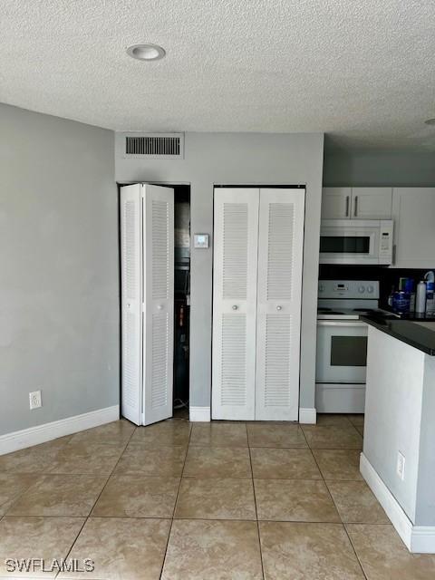 142 Santa Clara Dr Unit 7, Naples, FL 34104 - kitchen with a textured ceiling, visible vents, dark countertops, white cabinets, and white appliances
