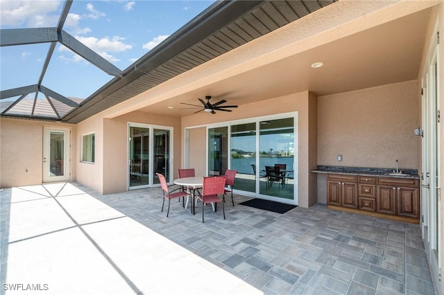 view of patio featuring outdoor dining area, a sink, a ceiling fan, and glass enclosure