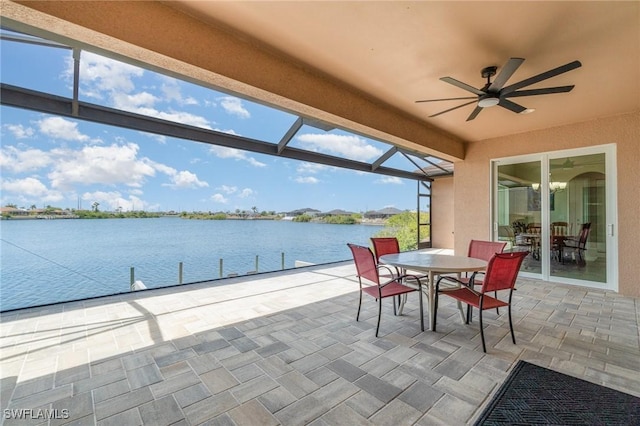 view of patio with a boat dock, a water view, glass enclosure, outdoor dining space, and a ceiling fan