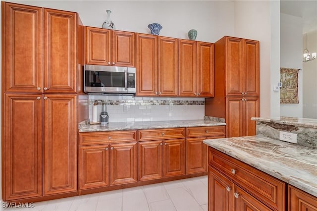 kitchen with light stone countertops, decorative backsplash, brown cabinetry, and stainless steel microwave