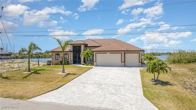 mediterranean / spanish house with decorative driveway, a water view, a tile roof, a front yard, and an attached garage
