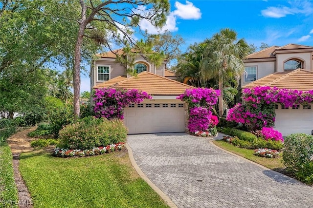 mediterranean / spanish-style house featuring decorative driveway, a tiled roof, and a garage