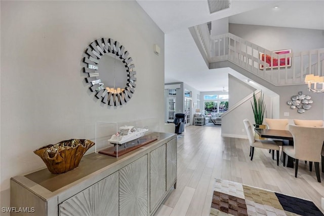 hallway featuring stairway, light wood-type flooring, baseboards, visible vents, and a high ceiling