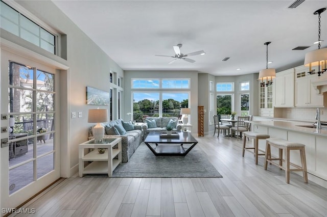 living room with ceiling fan with notable chandelier, visible vents, baseboards, and light wood-style floors