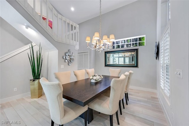 dining space featuring light wood-type flooring, a high ceiling, a notable chandelier, and baseboards