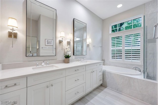 bathroom with tiled bath, double vanity, and a sink
