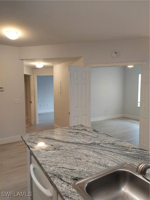 kitchen with light wood-type flooring, stainless steel dishwasher, baseboards, and a sink