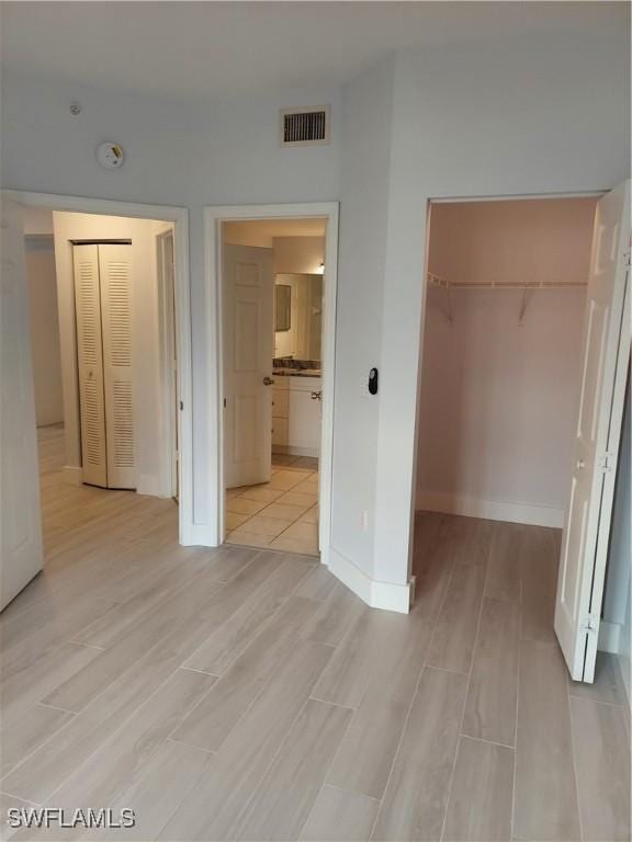 unfurnished bedroom with light wood-style flooring, baseboards, visible vents, a spacious closet, and a closet