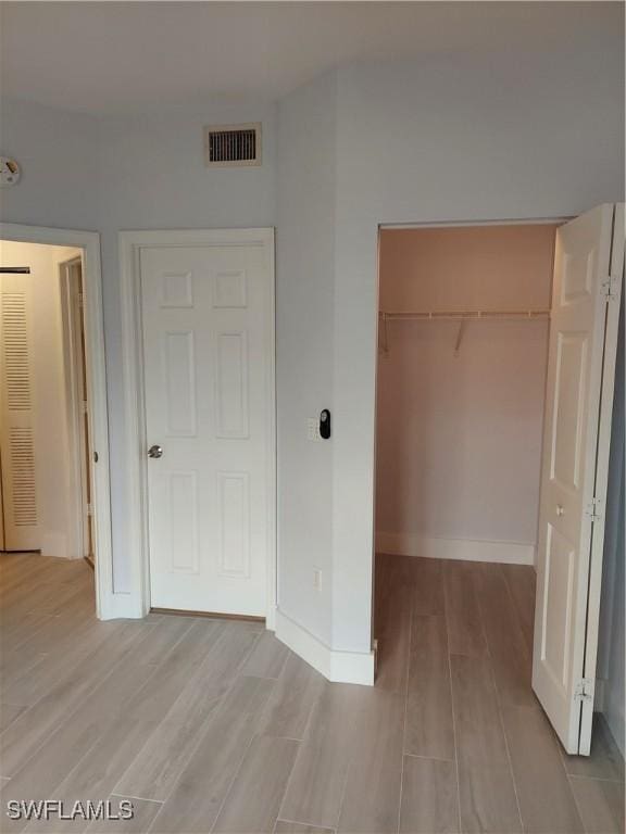 unfurnished bedroom with light wood finished floors, visible vents, a walk in closet, a closet, and baseboards