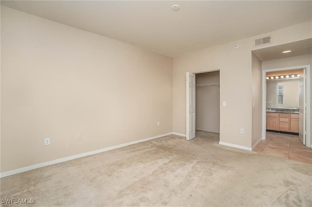 unfurnished bedroom featuring baseboards, visible vents, connected bathroom, and light colored carpet