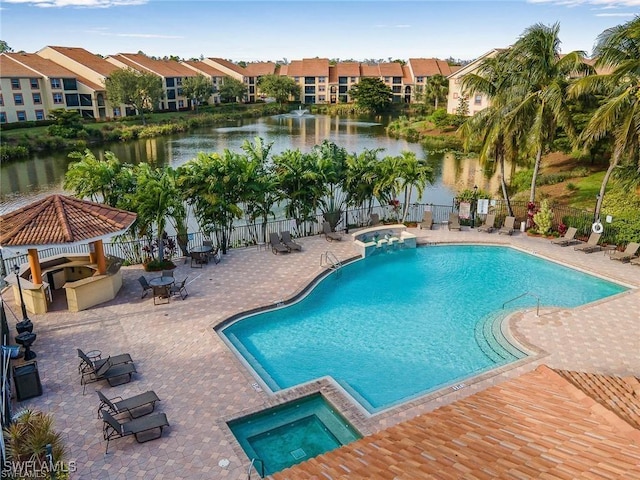 community pool featuring fence, a water view, a patio area, and a hot tub
