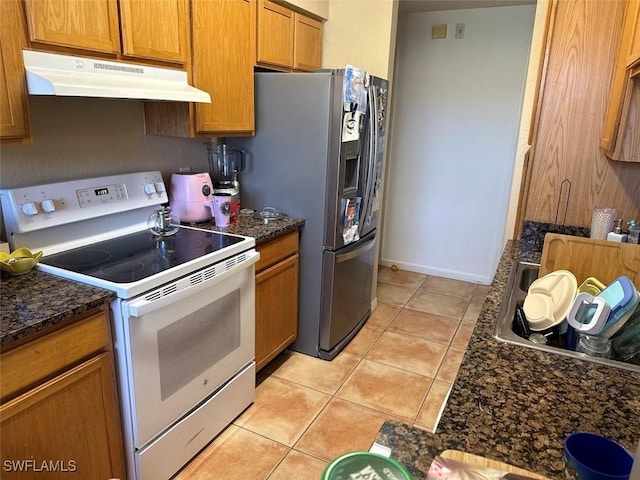 kitchen with white electric range oven, light tile patterned floors, brown cabinets, under cabinet range hood, and stainless steel fridge