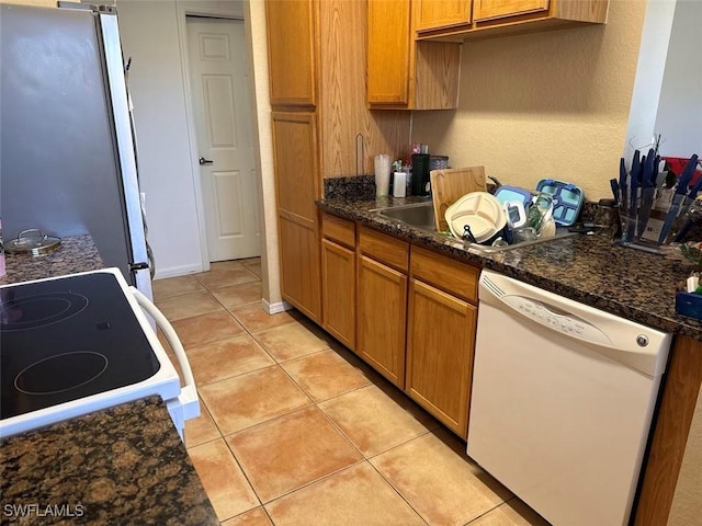 kitchen with light tile patterned floors, brown cabinets, freestanding refrigerator, white dishwasher, and range with electric stovetop