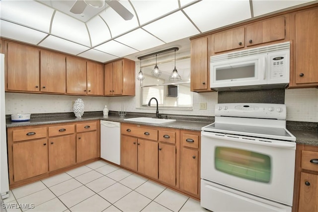 kitchen with tasteful backsplash, white appliances, brown cabinetry, dark countertops, and a sink
