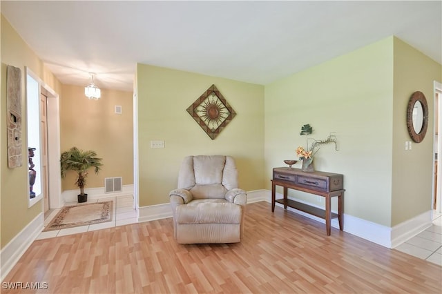 sitting room featuring baseboards, visible vents, light wood-type flooring, and an inviting chandelier