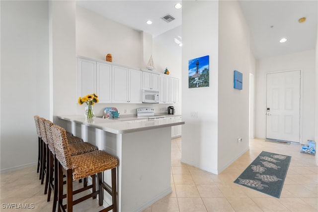 14524 Abaco Lakes Dr Unit 203, Fort Myers, FL 33908 - kitchen with white appliances, light tile patterned flooring, visible vents, a towering ceiling, and white cabinets