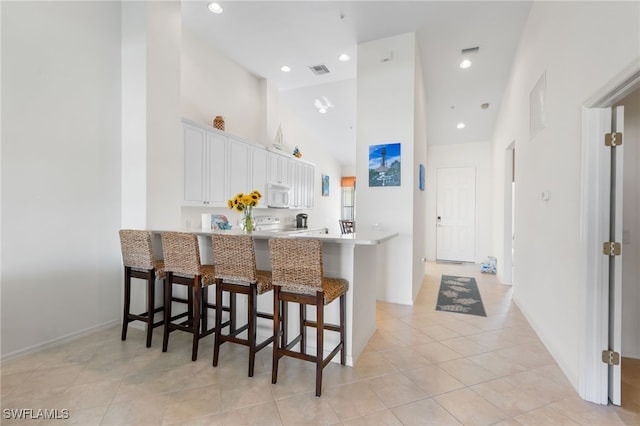 14524 Abaco Lakes Dr Unit 203, Fort Myers, FL 33908 - kitchen with a peninsula, white microwave, a kitchen breakfast bar, high vaulted ceiling, and white cabinetry