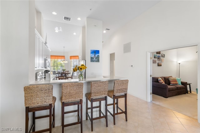 14524 Abaco Lakes Dr Unit 203, Fort Myers, FL 33908 - kitchen featuring a breakfast bar, visible vents, white cabinetry, a peninsula, and high vaulted ceiling