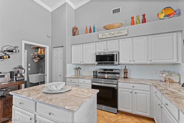 2640 SW 29th Ave, Cape Coral, FL 33914 - kitchen featuring appliances with stainless steel finishes, crown molding, decorative backsplash, a high ceiling, and white cabinetry