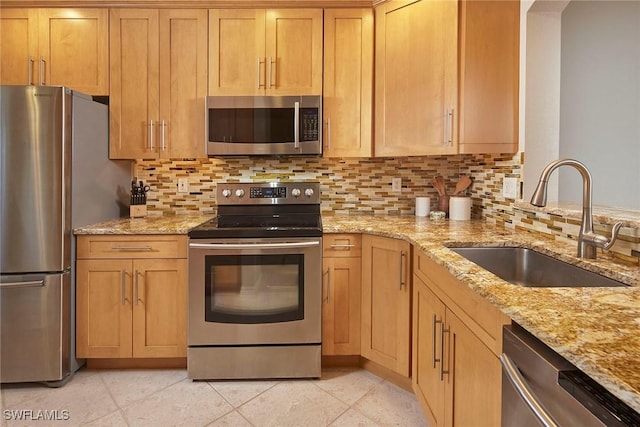 kitchen featuring appliances with stainless steel finishes, tasteful backsplash, a sink, and light stone countertops