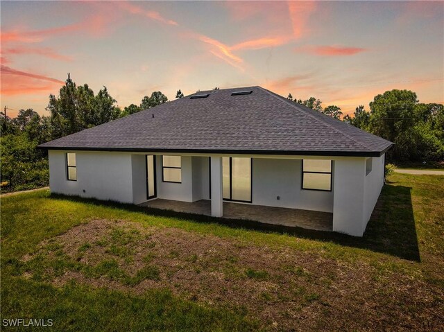 1025 Gladys St, Lehigh Acres, FL 33974 - back of property at dusk featuring roof with shingles, a yard, and stucco siding