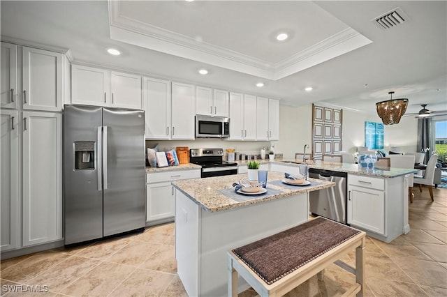 kitchen with stainless steel appliances, a peninsula, a tray ceiling, a sink, and visible vents