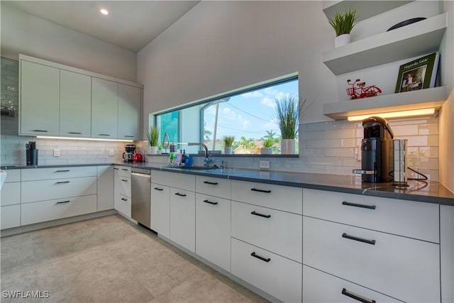 kitchen featuring open shelves, a sink, stainless steel dishwasher, decorative backsplash, and dark countertops