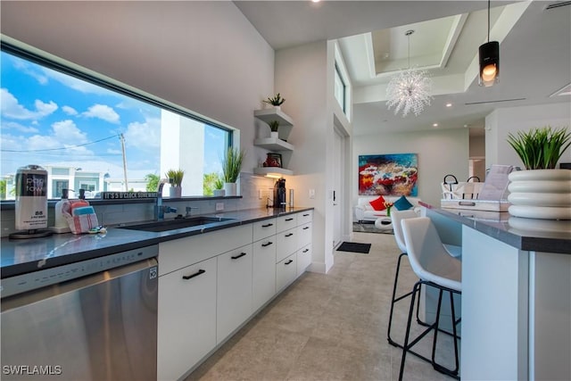 kitchen with stainless steel dishwasher, dark countertops, a sink, a kitchen breakfast bar, and white cabinets