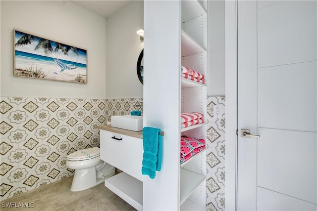 half bath featuring toilet, vanity, tile walls, a wainscoted wall, and tile patterned floors