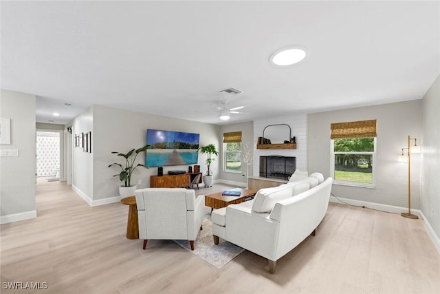 living area featuring light wood-style floors, a large fireplace, baseboards, and a ceiling fan