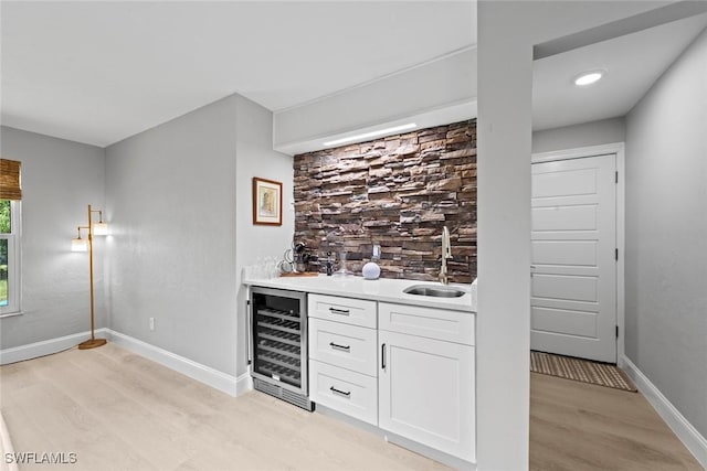 bar with wine cooler, indoor wet bar, light wood-style floors, baseboards, and a sink