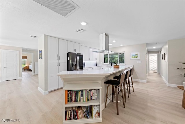 kitchen with visible vents, island range hood, light countertops, white cabinets, and stainless steel fridge with ice dispenser