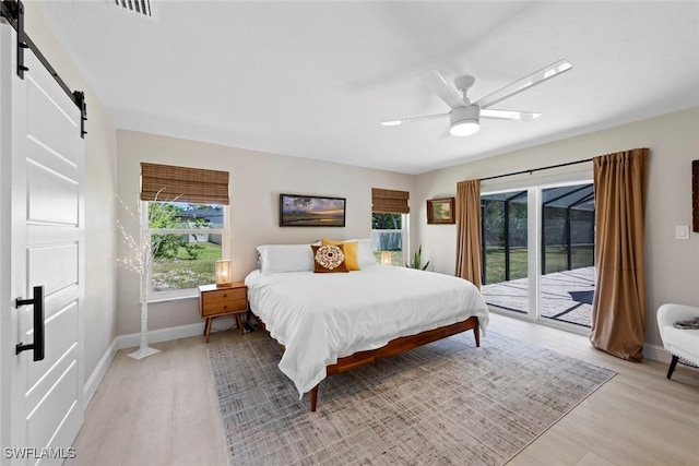 bedroom featuring visible vents, baseboards, access to outside, a barn door, and light wood-style flooring