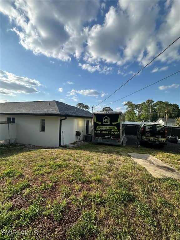 rear view of house with a lawn, fence, and stucco siding