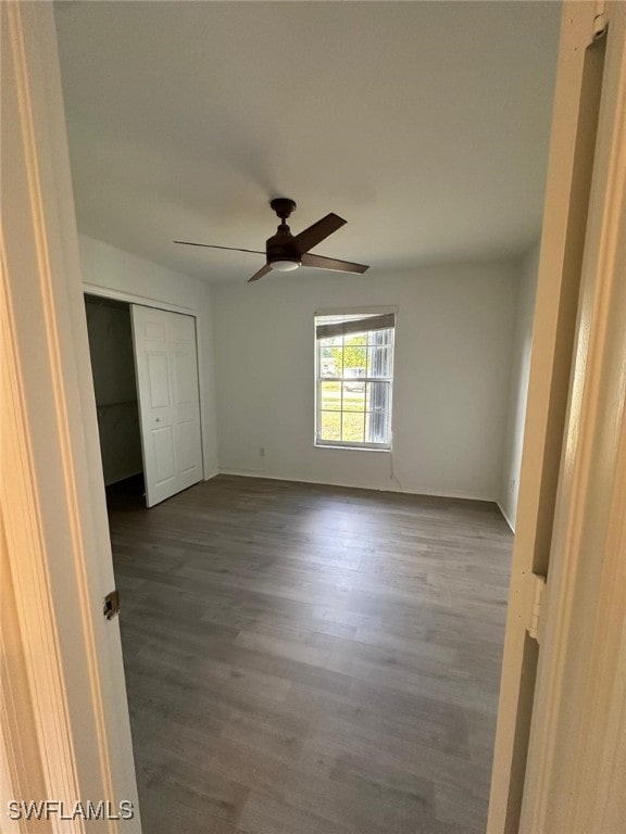 unfurnished bedroom featuring a closet, dark wood-style flooring, ceiling fan, and baseboards