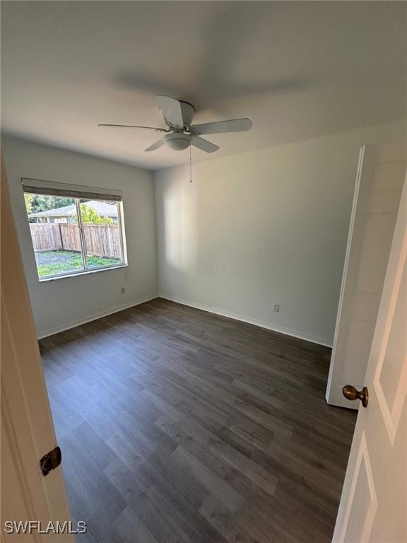 spare room featuring baseboards, ceiling fan, and dark wood finished floors