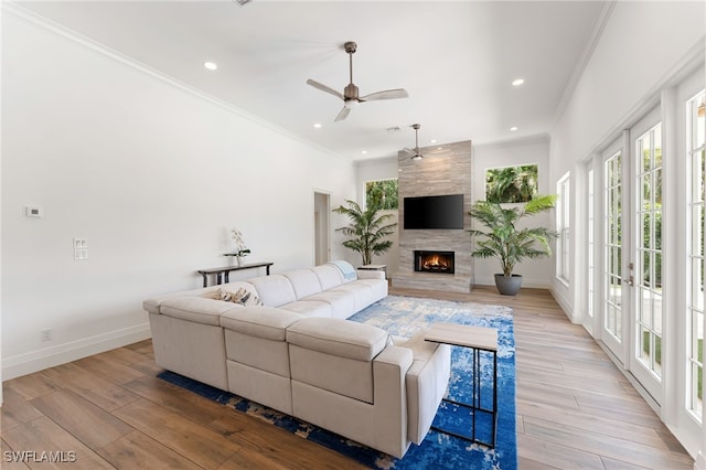 living room featuring crown molding, baseboards, ceiling fan, light wood-style floors, and a fireplace