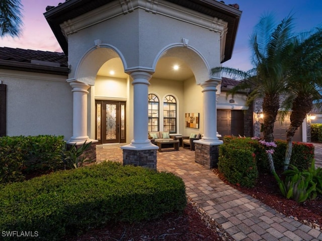 exterior entry at dusk featuring a porch, a garage, and stucco siding
