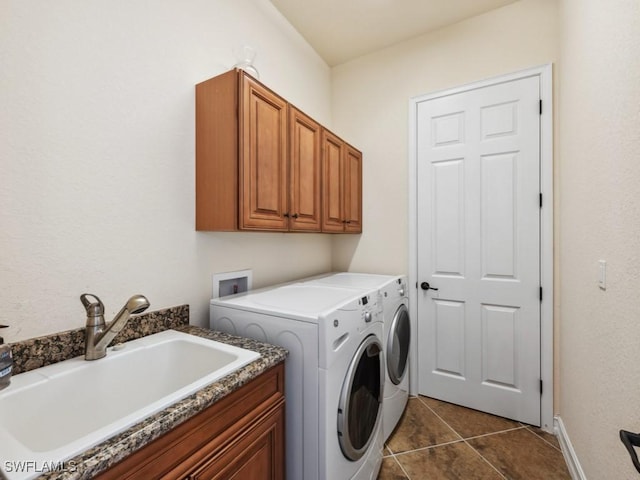 washroom with a sink, cabinet space, washer and clothes dryer, baseboards, and dark tile patterned flooring