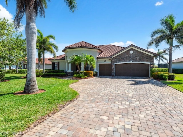 mediterranean / spanish house featuring stone siding, a tiled roof, decorative driveway, a front yard, and a garage
