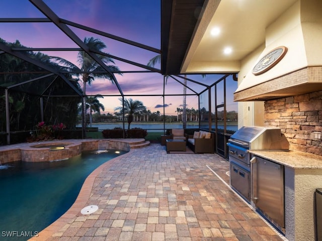 patio terrace at dusk featuring a pool with connected hot tub, an outdoor living space, exterior kitchen, glass enclosure, and grilling area