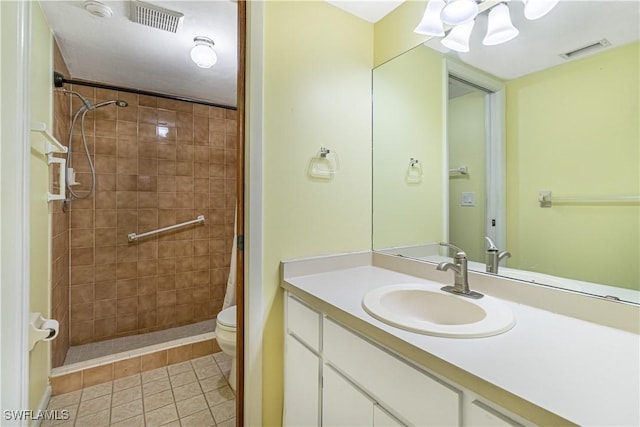 bathroom with tile patterned flooring, toilet, tiled shower, and vanity