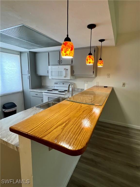 2241 E 5th St Unit 103, Lehigh Acres, FL 33936 - kitchen with white appliances, dark wood finished floors, a kitchen breakfast bar, baseboards, and a peninsula