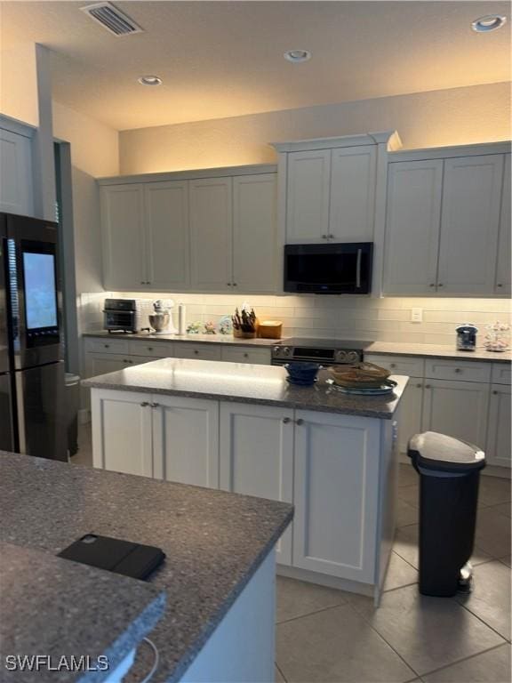 kitchen with dark stone counters, tasteful backsplash, black appliances, and visible vents