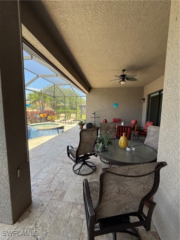 view of patio / terrace with glass enclosure, ceiling fan, a pool with connected hot tub, and outdoor dining area